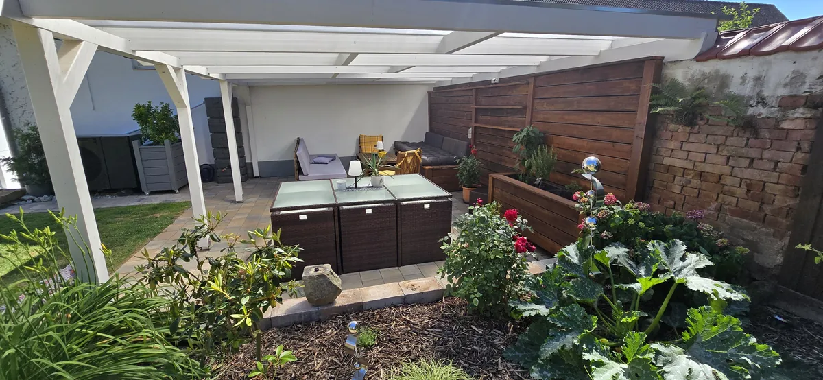 Überdachte Terrasse mit Rattan-Sitzgruppe, Lounge-Ecke und Blumenbeet im Relax-Garten